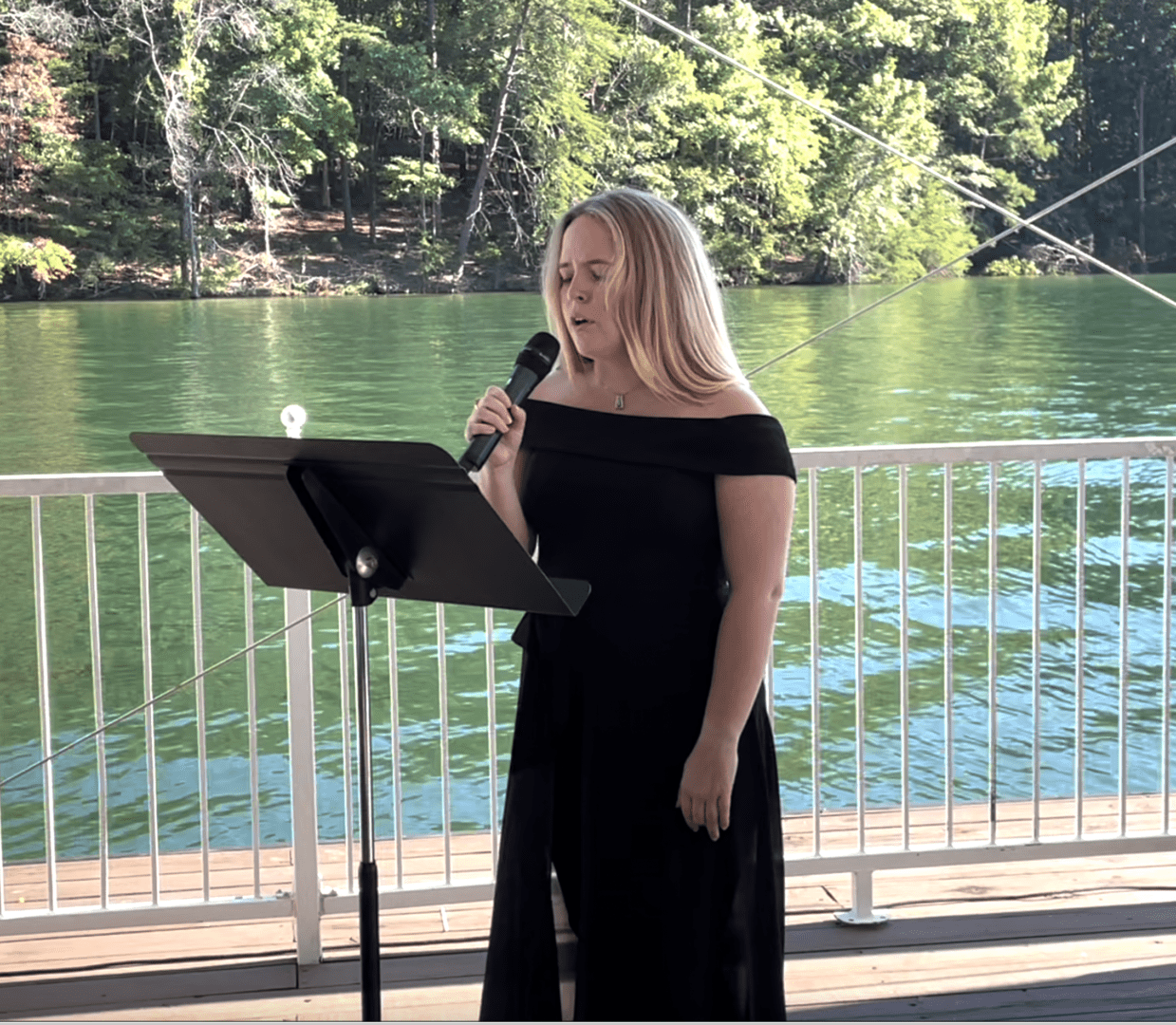 a lady in a black dress singing near a river